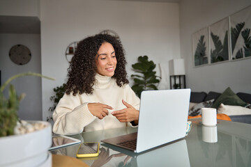 Young woman, female latin employee using laptop remote working at home office looking at computer...
