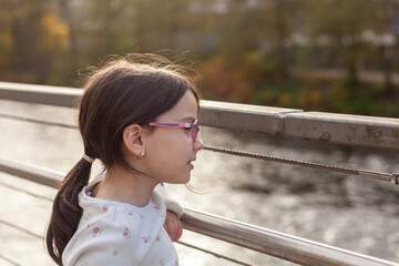 little girl with glasses on the bridge over the river, autumn day