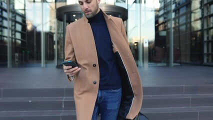 Successful young businessman leaving building office after workday using mobile phone to make a call outdoors. Salesman talking on smartphone at city street. Business and technology concept.