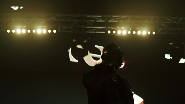 African-American Black rap artist performing his gig on a stage of a large venue, surrounded by bright flashig lights