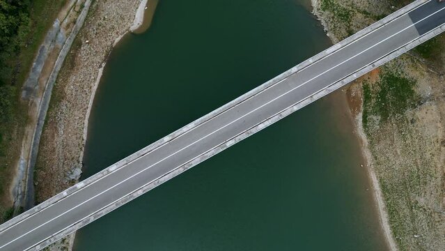 Aerial view of a bridge over a river, the road diagonally separates the image in half, two motorcycles crossing the frame, the water in the river moves gently. 