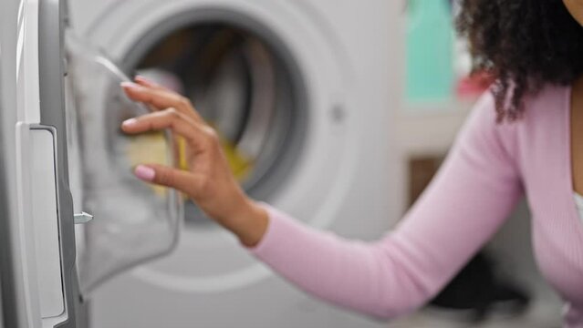 African american woman washing clothes putting detergent bag on washing machine at laundry room