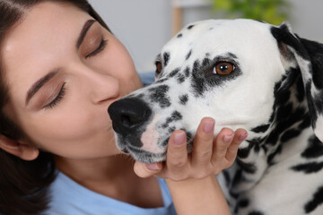 Beautiful woman kissing her adorable Dalmatian dog indoors, closeup. Lovely pet