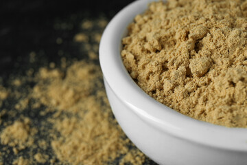 Bowl of mustard powder on black table, closeup. Space for text