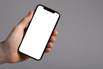 Obraz na płótnie Canvas Man holding smartphone with blank screen on light grey background, closeup. Mockup for design
