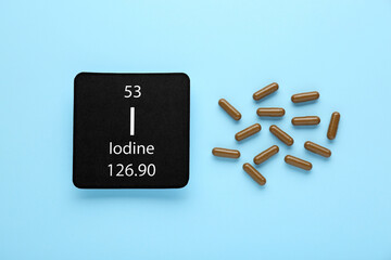 Card with iodine element and pills on light blue background, flat lay