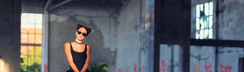 	
Goth ballerina holding parasol and wearing sunglasses posing in abandoned building