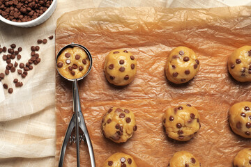 Uncooked chocolate chip cookies and scoop on parchment, flat lay