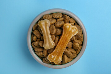Dry dog food and treats (chew bones) on light blue background, top view
