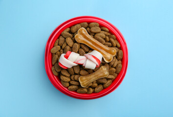 Dry dog food and treats (chew bones) on light blue background, top view