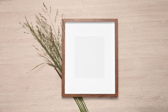 Empty photo frame and beautiful wildflowers on wooden background, flat lay. Mockup for design