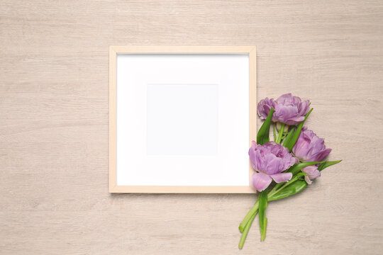 Empty photo frame and beautiful tulip flowers on wooden background, flat lay. Mockup for design