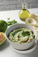 Delicious guacamole and ingredients on white table