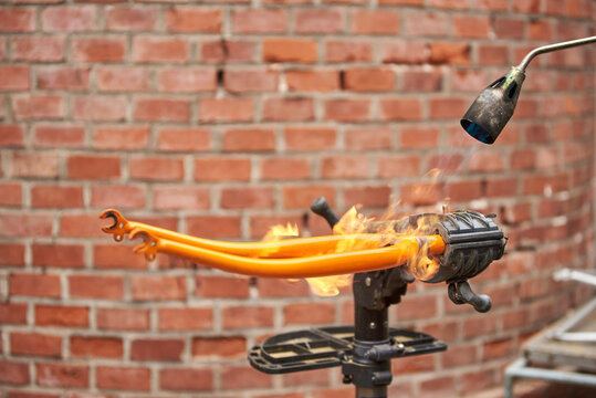 Use of a blowtorch to remove the paint of an orange fork from a bicycle that is being renovated in a bike workshop.