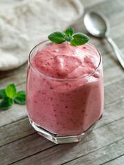 Healthy Strawberry or Raspberry Cream mousse in glass on a wooden table with mint leaves and spoon. Delisious summer dessert. Top view, close up, vertical