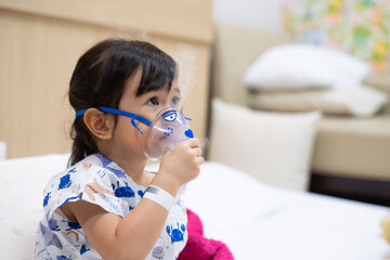 Little asian girl sick making inhalation with nebulizer to reduce coughing and sputum in the neck ,...