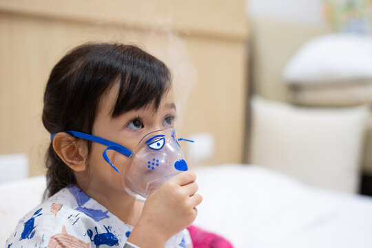Little asian girl sick making inhalation with nebulizer to reduce coughing and sputum in the neck , lying in bed at hospital, child taking medication while breathing in through face mask
