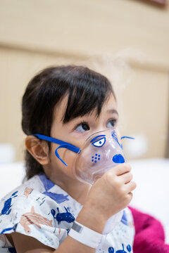 Little asian girl sick making inhalation with nebulizer to reduce coughing and sputum in the neck , lying in bed at hospital, child taking medication while breathing in through face mask