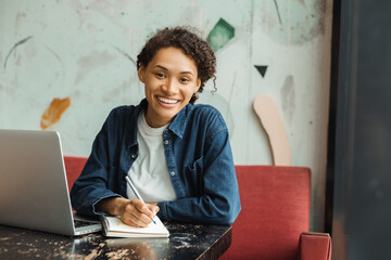 Portrait of smiling beautiful African American woman, successful writer taking notes looking at...