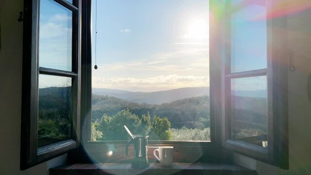 Steaming coffee maker and a cup on a window sill with hills in the background