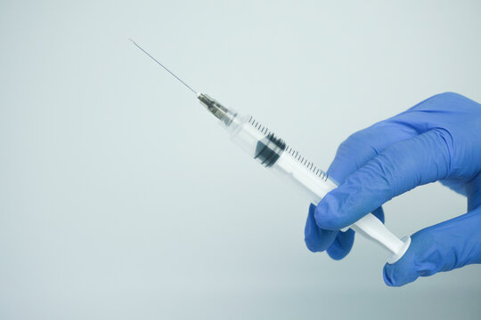 Male hand in blue gloves holding a plastic syring with liquid for injection isolated on white background. Health care, treatment concept