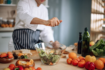 The professional master chef prepares a bowl of various types of fruit and vegetable salad with great passion and enthusiasm. Expertly mix all the ingredients and materials with care and precision.