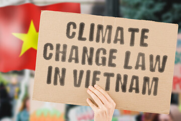 The phrase " Climate change law in Vietnam " on a banner in men's hand with blurred Vietnami flag on the background. Environment protection. Nature. Legislation. Rules. Policy