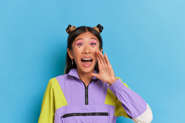 Funny Thai girl in sportswear stands on blue background, holding her hands as if she's screaming, time to buy concept, copy space