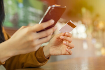Hands of young asian woman holding credit card and mobile phone for electronic payment in internet online with sunlight.