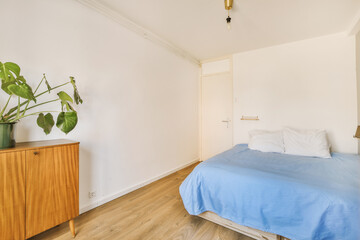 a bedroom with a bed, dresser and plant on the side table in front of the door to the room