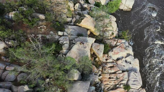 young male hiker laying down on a large boulder relaxing and taking in the sunset on the kern valley river in Kernville California aerial orbit
