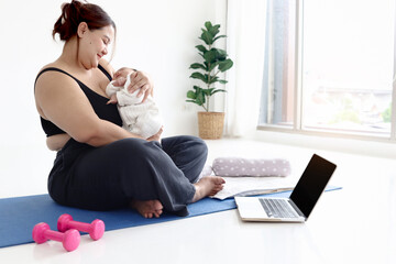 Plump mother doing exercises while watching online tutorial on laptop, overweight chubby mom with fat body after childbirth workout at home try to lose weight while raising infant newborn baby child.