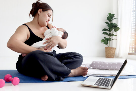 Busy plump mother raising infant newborn baby child while doing exercises while watching online tutorial on laptop, overweight chubby mom with fat body after childbirth workout try to lose weight.