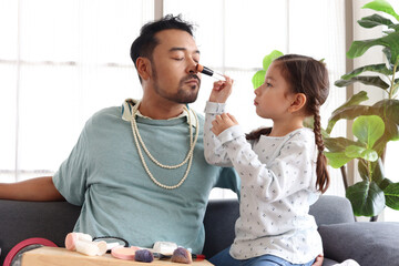 Joyful father playing with his little cute daughter together, girl doing makeup to her dad by...