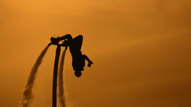 Epic scene at sunset. Silhouette of a flyboarder against the backdrop of the setting sun and sky. The athlete does somersaults in the air