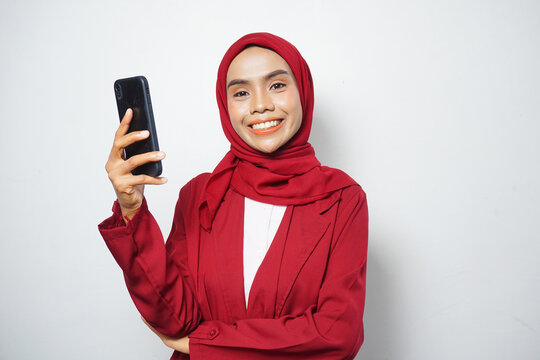 Asian Muslim businesswoman in red casual holding a smartphone isolated by a white background - Powered by Adobe