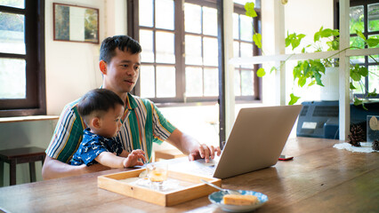 Boy playing with dad holding  while working on laptop sitting in coffee cafe