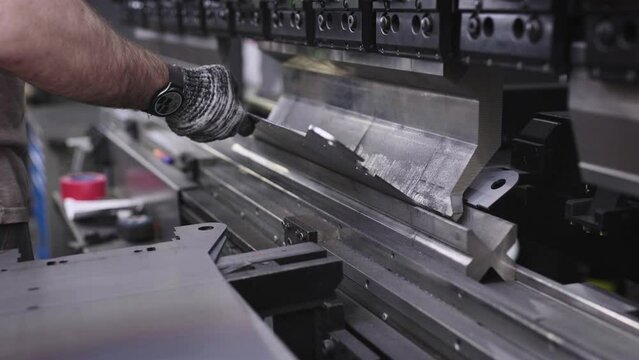 A close-up shot shows a worker's hands at a manufacturing plant, bending steel parts on a specialized machine. The workshop specializes in metalworking