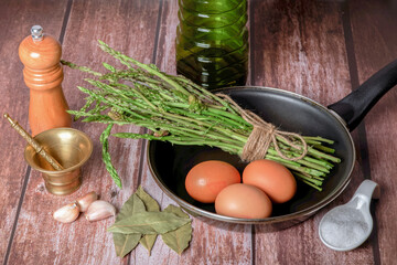 bunch of wild asparagus in a frying pan with eggs, garlic, olive oil and pepper, ingredients to make an omelet.