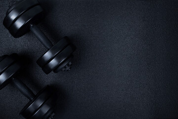 Top view of black dumbbells weights on textured mat background. Flat lay. Fitness or bodybuilding sport training concept. Copy space. - obrazy, fototapety, plakaty