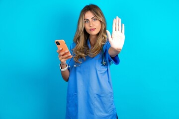Young caucasian blonde doctor woman wearing blue uniform using and texting with smartphone with...