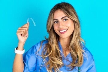 Young caucasian blonde doctor woman wearing blue uniform holding an invisible braces aligner,...