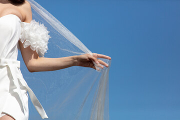Fototapeta na wymiar A woman's hand with a white wedding veil against a blue sky