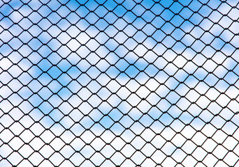 Chain link fence against the blue sky and clouds. Abstract background