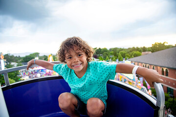 A cute African American little boy enjoying a Ferris Wheel ride at a local carnival during on a summer evening