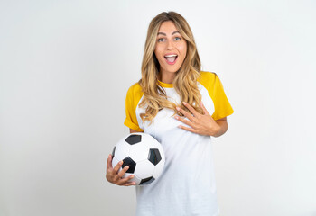 Young beautiful woman wearing football T-shirt over white background smiles toothily cannot believe eyes expresses good emotions and surprisement