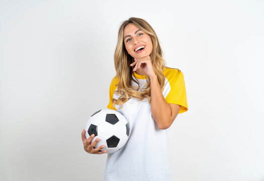 Young beautiful woman wearing football T-shirt over white background laughs happily keeps hand on chin expresses positive emotions smiles broadly has carefree expression