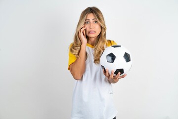 Afraid funny Young beautiful woman wearing football T-shirt over white background holding telephone and bitting nails