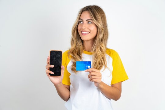 Young beautiful woman wearing football T-shirt over white background holding bank card modern device looking empty space