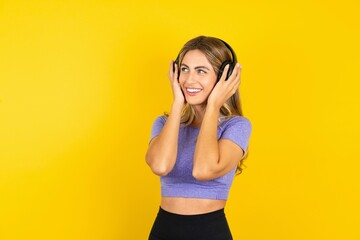 Naklejka premium Young beautiful blonde woman wearing sportswear over yellow studio background wears stereo headphones listens music concentrated aside. People hobby lifestyle concept